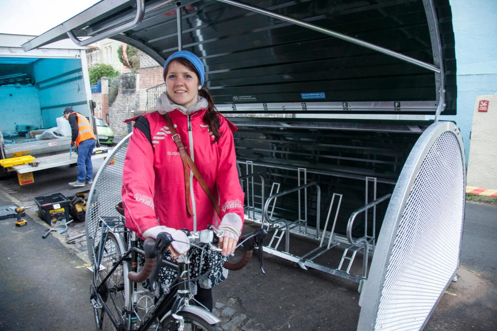 Woman standing near an open bike hangar holding a bike