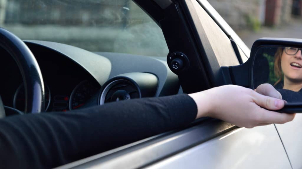 Image of a drivers side window in a car open with a lady adjusting the wing mirror.