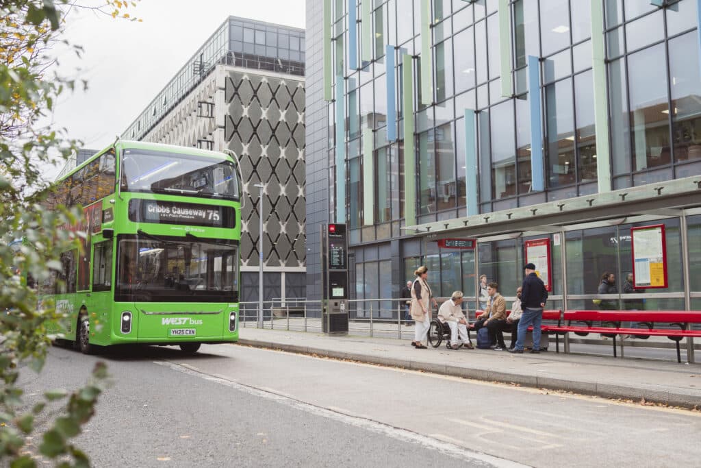A green WEST bus traveling past a metrobus stop in Bristol City Centre