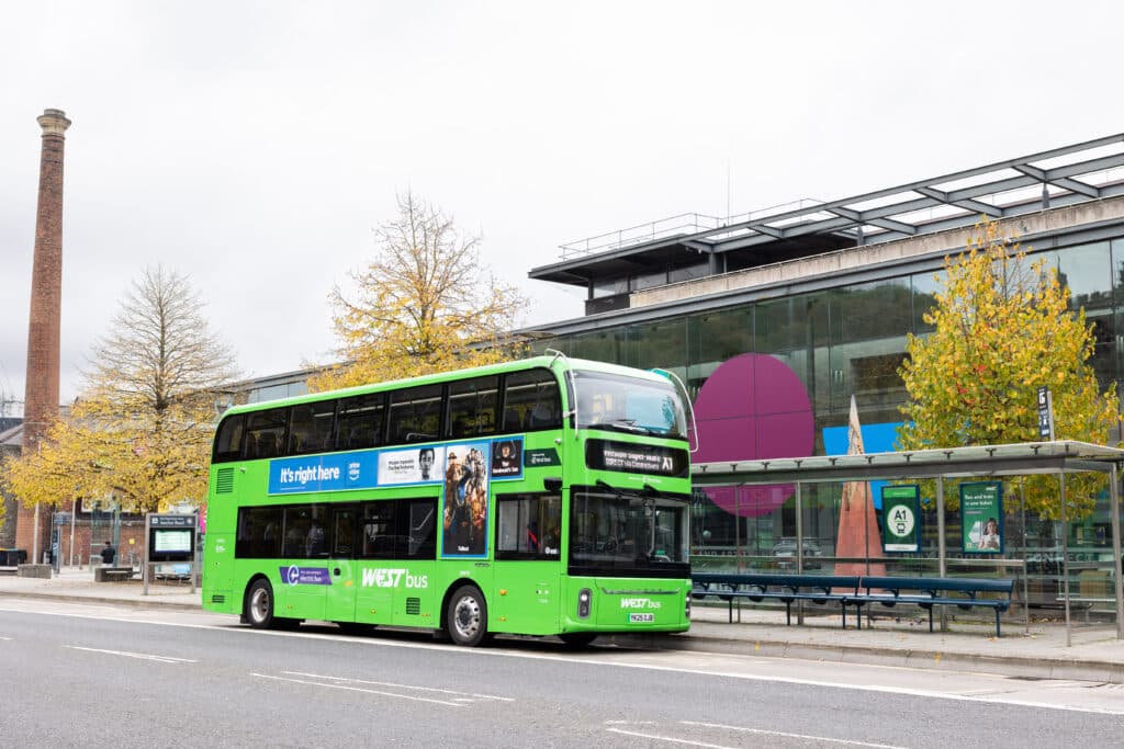 A green WEST bus stopped outside a bus stop next to "We are the Curious" in Bristol City Centre