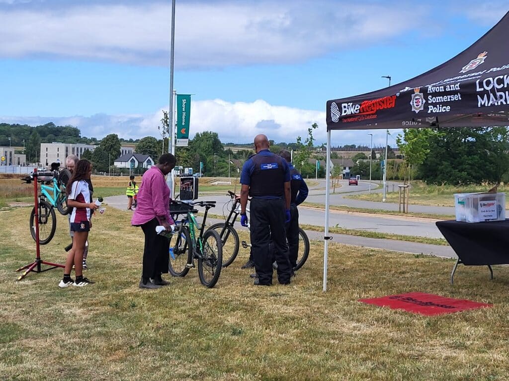 Photo of a sustainable travel roadshow at Beaufort Park showing police bike marking, and Dr Bike offering cycle checks