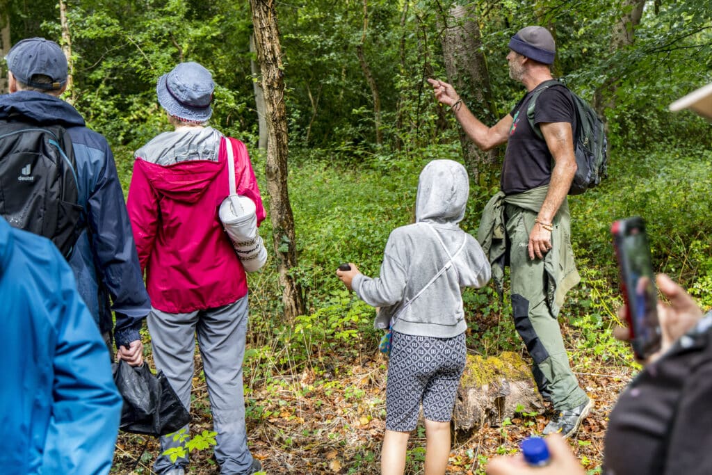 Photo of the walk leader highlighting interesting natural features on a tree to a group of attendees in Crossways Wood.