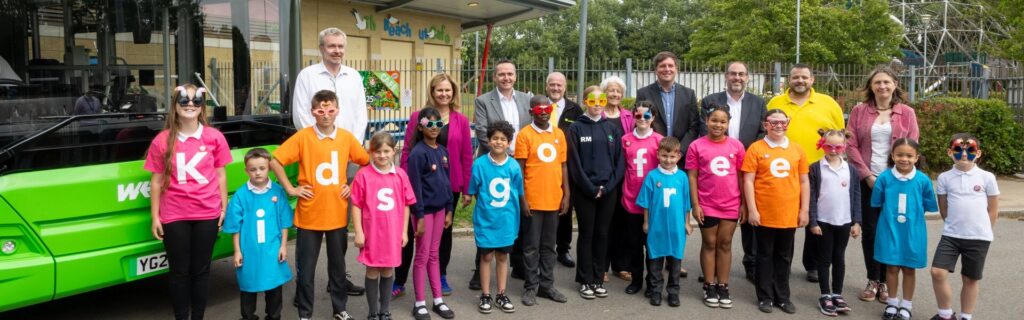 Image of adults and kids lined up infront of a bus with the kids t-shirts spelling out "kids go free"