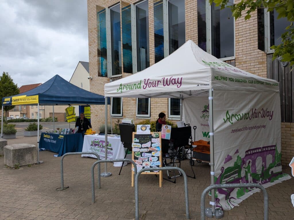 Photo of two pop-up gazebos outside the community centre featuring a face painting activity in the foreground and a sustainable travel stall in the background.