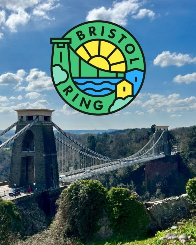 Bristol Ring logo over a scenic view of the Clifton Suspension Bridge in Bristol, England, under a bright blue sky with scattered clouds. The circular logo features stylized landmarks, a sunrise, water waves, and the text “BRISTOL RING.”
