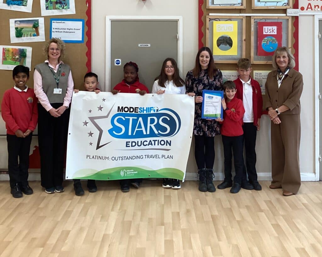 School teachers and children lined up in the school hall holding a giant poster with the ModeShift STARS Education award.