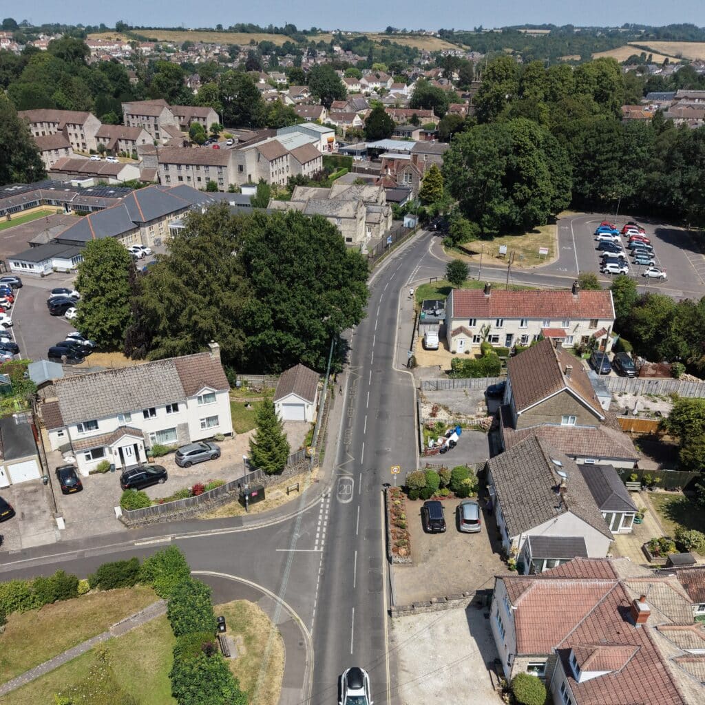 Aerial view of Midsomer Norton showing houses, parked cars, a car park, school and surrounding countryside