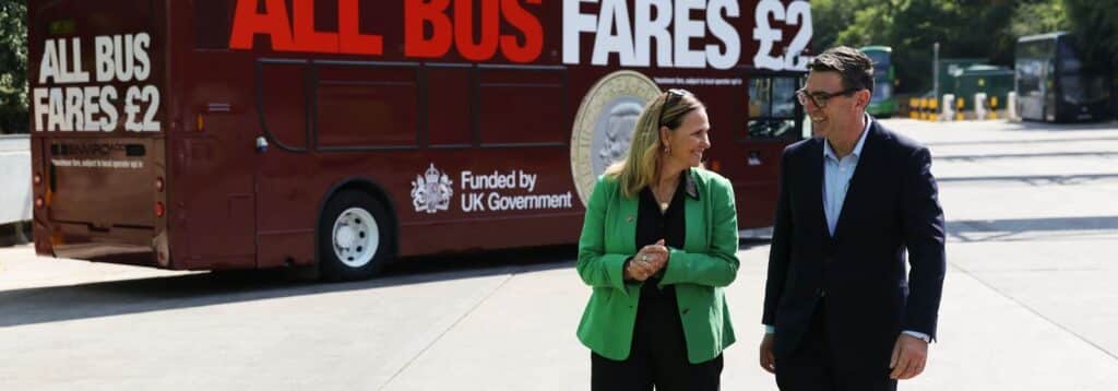 WoE Mayor Helen Godwin and Prime Minister Andy Burnham stood in front of a double decker bus with livery advertising the new £2 bus fare cap